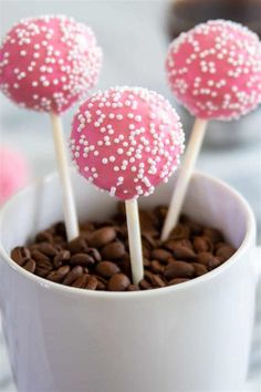 three pink cake pops sitting on top of a white cup filled with chocolate chips and sprinkles