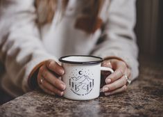 a woman holding a white and black coffee mug