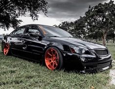 a black car with orange rims parked in the grass