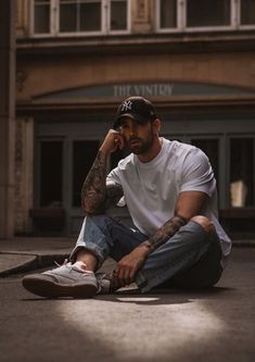 a man sitting on the ground talking on a cell phone with his hand to his ear