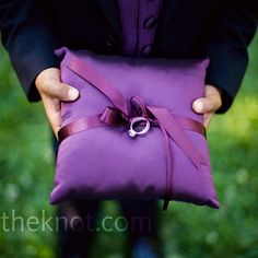 a person holding a purple pillow with a ring on it's end and a pink ribbon around the edge