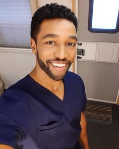 a man with a goatee smiles while sitting in front of a door on an airplane