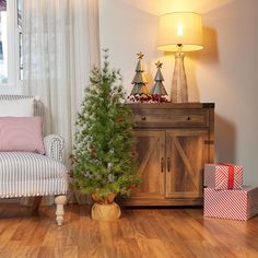 a small christmas tree sitting in front of a wooden cabinet next to a white chair