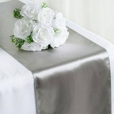 a bouquet of white flowers sitting on top of a satin table runner with greenery