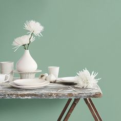 a table topped with white dishes and vases filled with flowers on top of a wooden table