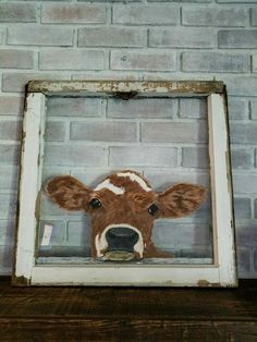 a brown and white cow sticking its head out of a window frame on a wooden table