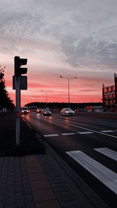 cars are driving down the road at dusk time with red and pink clouds in the background