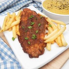 a white plate topped with chicken and french fries next to a bowl of soup on a table