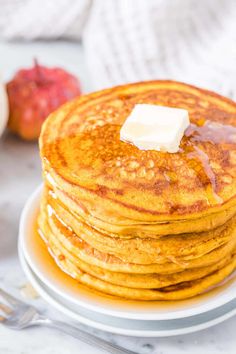 a stack of pancakes with butter and syrup on a white plate next to an apple