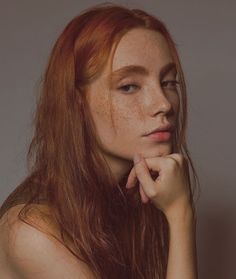 a woman with freckles on her face and hands near her chin looking to the side