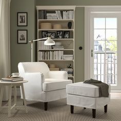 a white chair and ottoman in front of a bookshelf with open doors to another room