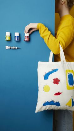 a woman holding a tote bag with paint and markers on it