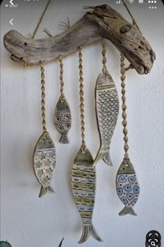 three fish hanging from chains on a wall next to a tree branch and some plants