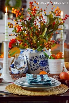 the table is set with blue and white dishes, plates, silverware, candlesticks and fruit