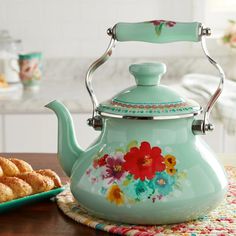 a tea kettle sitting on top of a wooden table next to some cookies and other food