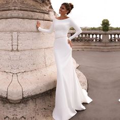 a woman in a white dress leaning against a stone wall and posing for the camera