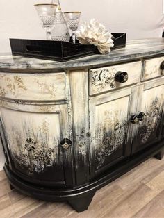 an old black and white dresser with flowers on it's sideboard, next to a glass vase