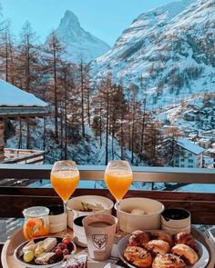 two glasses of orange juice and some food on a table with mountains in the background