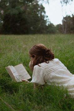 a woman laying in the grass reading a book