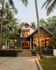 a house that is surrounded by palm trees and lights in the front yard, with steps leading up to it