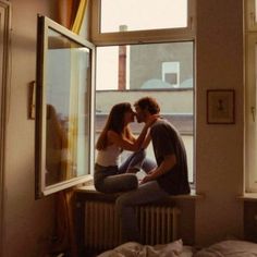 two people sitting on a window sill in front of a window and one person kissing the other