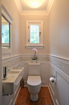 a white toilet sitting in a bathroom next to a sink under a window with a flower on the tank