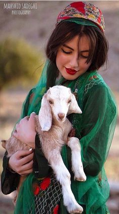 a woman holding a baby goat wearing a green dress and a red headband with her eyes closed