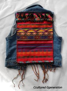 a denim vest with colorful stripes and fringes on the back, sitting on top of a white sheet