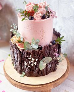 a three tiered cake with pink frosting and fresh flowers on top, sitting on a wooden stand