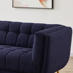 a blue couch sitting on top of a hard wood floor next to a framed painting