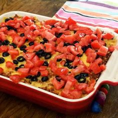 a casserole dish with tomatoes, black olives and cheese in it on a wooden table