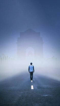 a man walking down the road in front of an arch on a foggy day