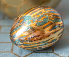 an artistically painted egg sitting on top of a blue and brown table cloth next to two vases