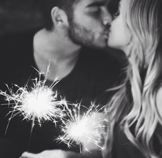 a man and woman kissing while holding sparklers