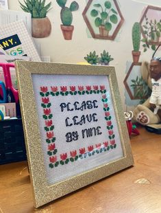 a cross stitch picture frame sitting on top of a wooden table next to a potted plant