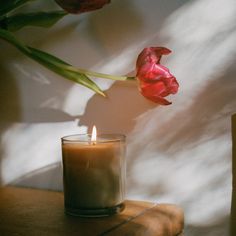 a candle and some flowers sitting on a table next to a vase with red tulips