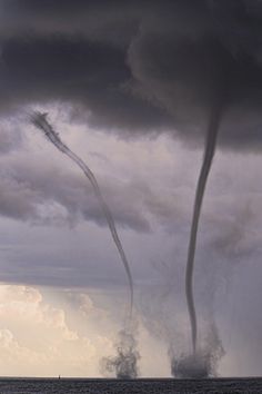 two jets are flying in the sky near some water and storm clouds, while another jet is coming up behind them