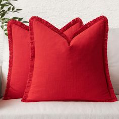 two red pillows sitting on top of a white couch next to a potted plant