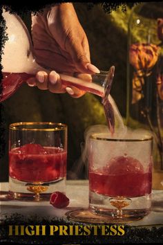 a person pouring liquid into a glass filled with ice and raspberries on top of a table