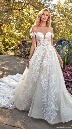 a woman in a white wedding dress standing on the ground with trees and bushes behind her