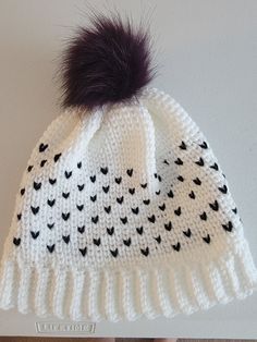 a white knitted hat with black birds and a purple pom - pom