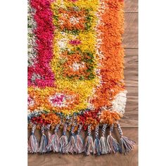 a multicolored rug with tassels and fringe on wooden floor next to wall