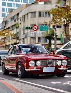 a red car driving down a street next to tall buildings