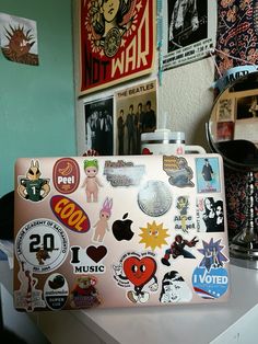 a laptop covered in stickers sitting on top of a white desk next to a lamp