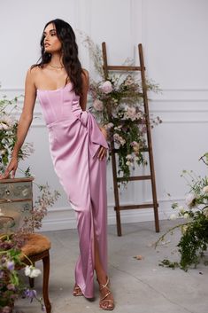 a woman in a pink dress standing next to a floral arrangement and holding a suitcase