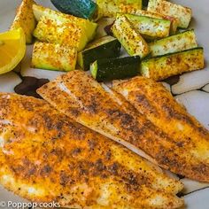 grilled fish, zucchini and squash on a white plate with lemon wedges