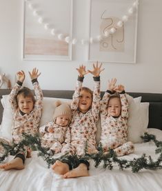 three children sitting on a bed with their arms in the air and wearing matching pajamas