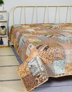 a bed with a quilt on top of it next to a book shelf and potted plant