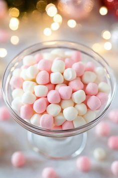 pink and white marshmallows in a glass dish on a table with christmas lights