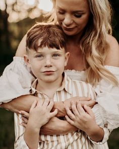 a woman holding a young boy who is wearing a white and brown striped shirt with his hands on his chest